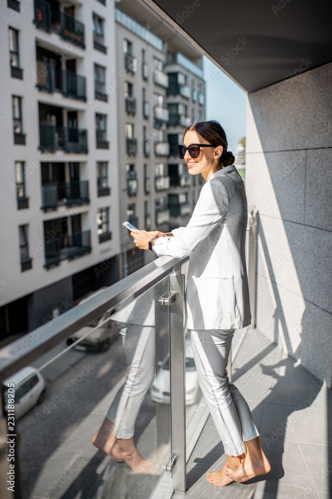 现代住宅公寓阳台上穿着白色西装、戴着墨镜的年轻商务女性