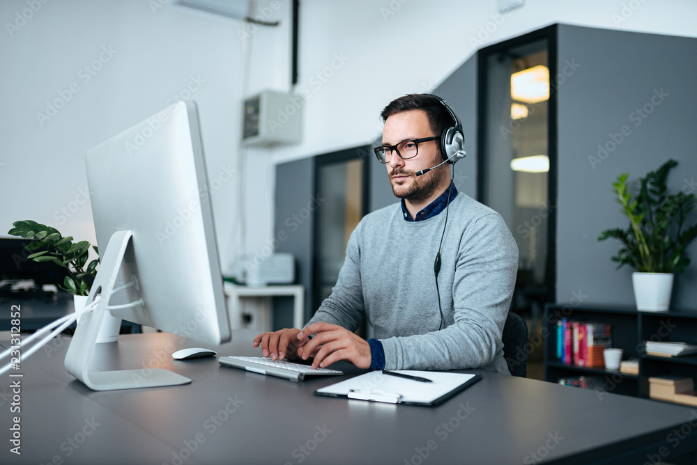 使用耳机在电脑上工作的年轻男性客户支持。