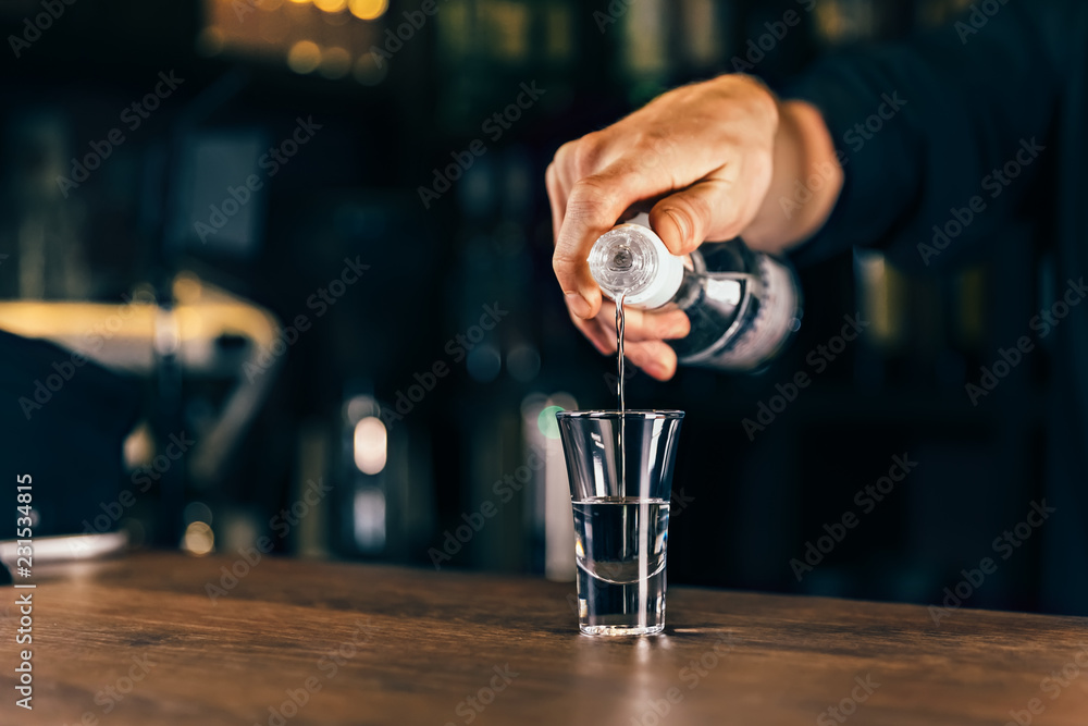 酒吧服务员拿着瓶子把饮料倒进玻璃杯。调酒师把烈性酒精饮料倒进s