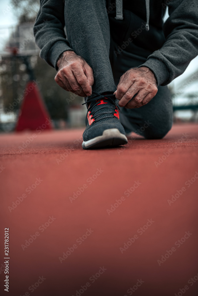 一名男子在田径场上系鞋带的照片。