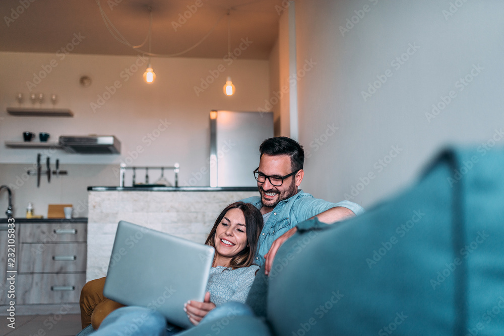 一对微笑的情侣在沙发上放松，看着笔记本电脑屏幕。