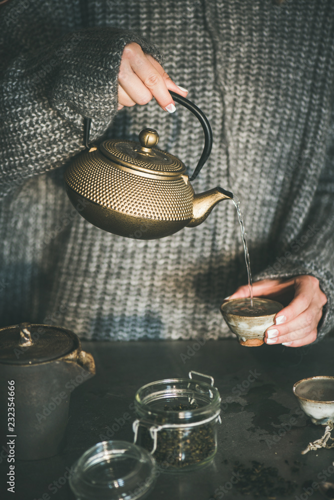 茶道。穿着灰色保暖针织冬衣的年轻女性从金色的铁锅里倒绿茶