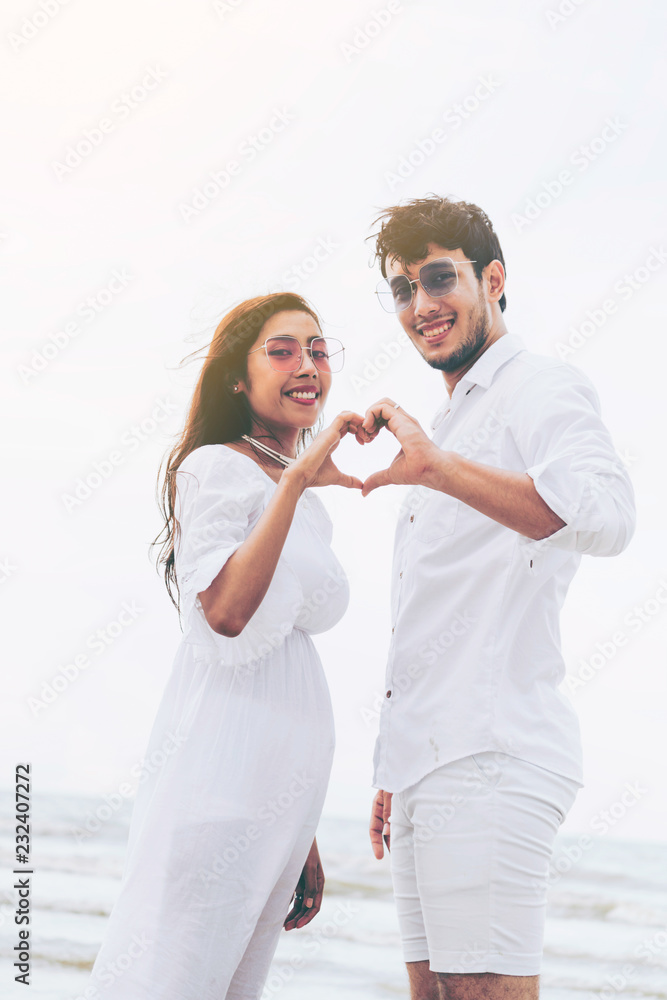 年轻情侣在夏天的海滩上展示心形手势。