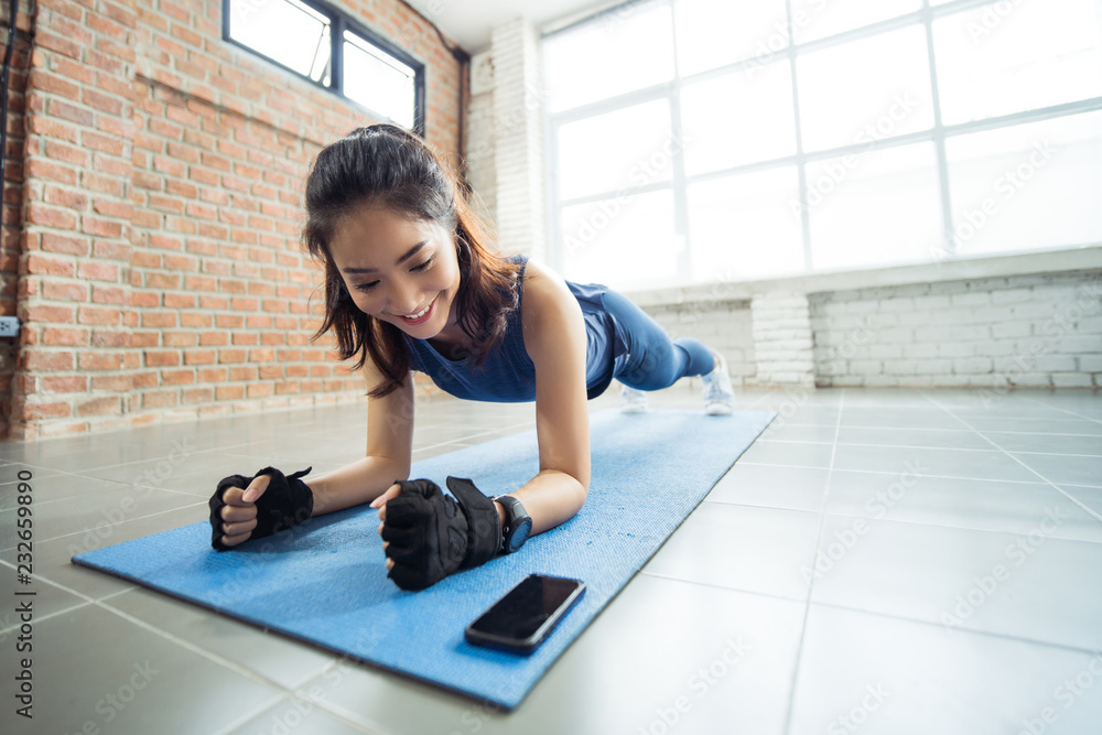 亚洲女性在健身房锻炼，她假装做平板运动。她在看电话