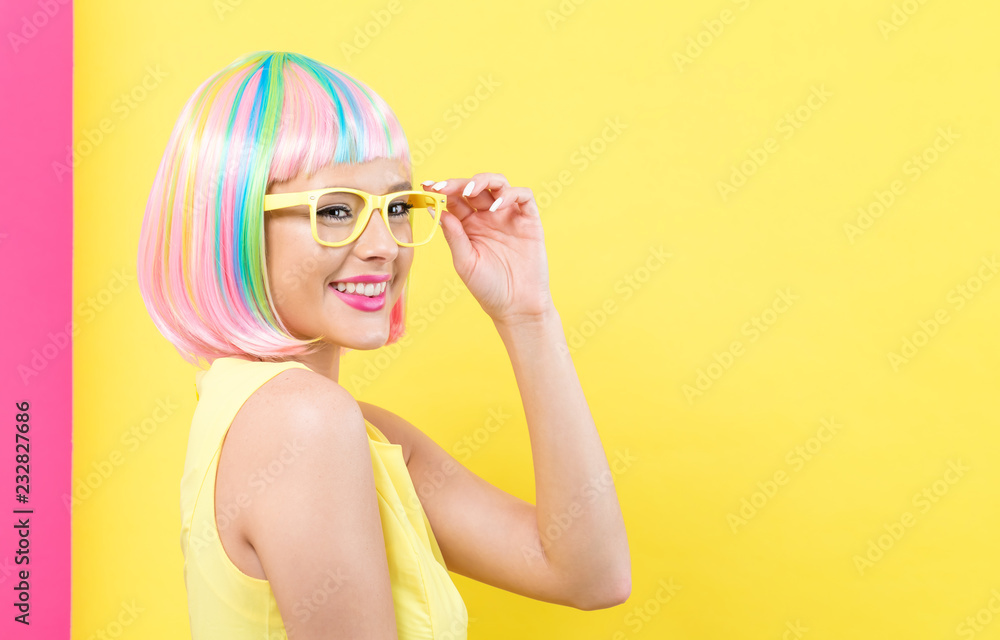 戴着彩色假发的年轻女子，黄色和粉色相间的背景上戴着太阳镜