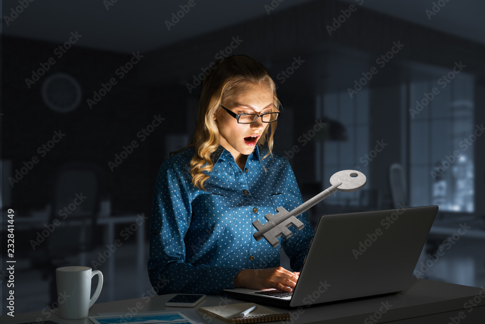 迷人的金发女郎戴着眼镜在黑暗的办公室里用笔记本电脑。混合媒体