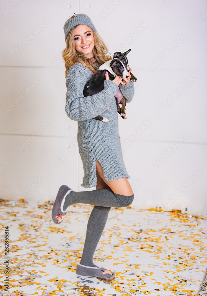 一个美丽的年轻女人抱着两只小狗。微笑的金发女郎穿着灰色连衣裙，手里拿着宠物