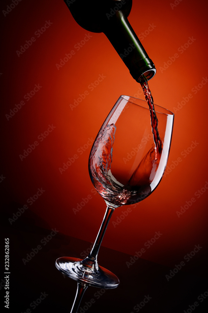在红色背景下将红酒倒入玻璃杯