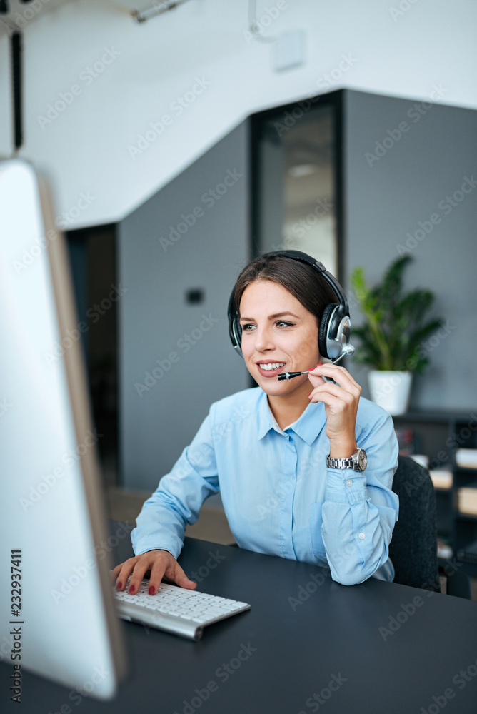 可爱的年轻优雅的女商人，戴着耳机在电脑上工作。