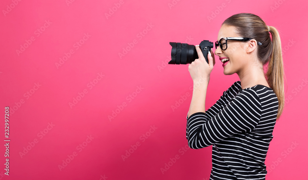 粉色背景下带着专业数码单反相机的年轻女性