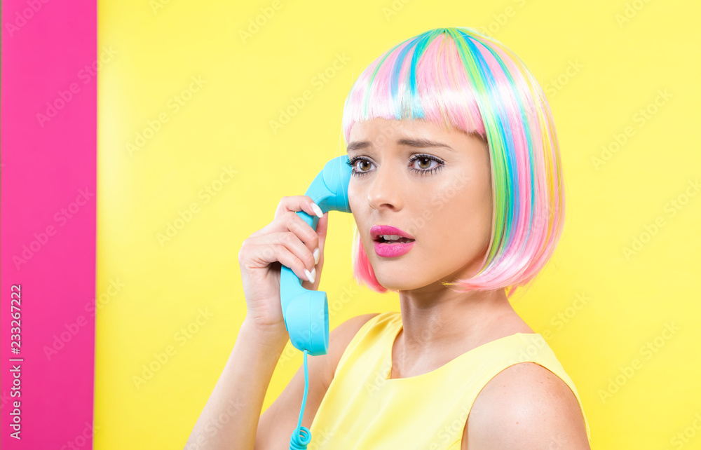戴着彩色假发的年轻女子在黄色和粉色的背景下用复古的电话交谈
