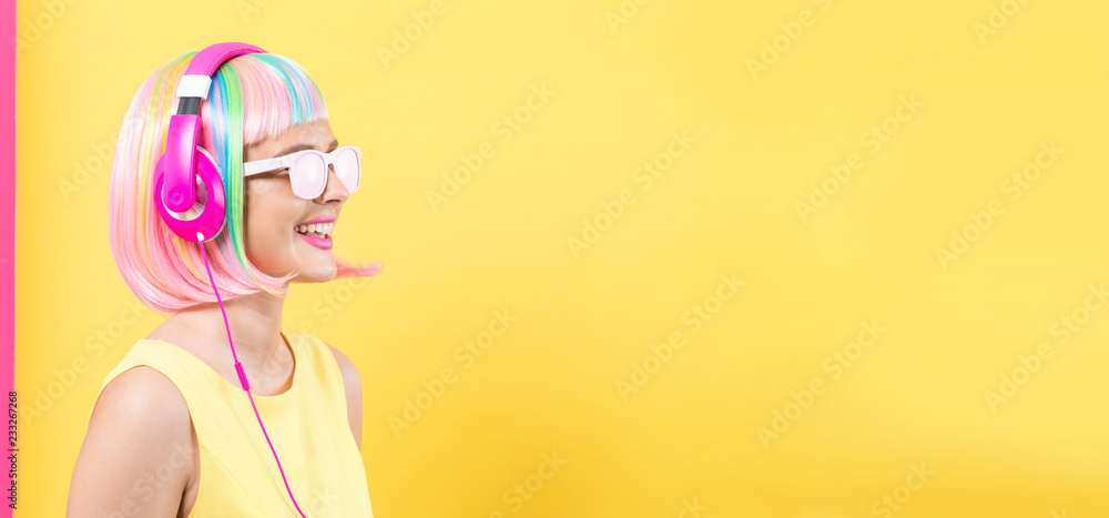 戴着彩色假发的女人，戴着耳机，在黄色和粉色的背景上听音乐