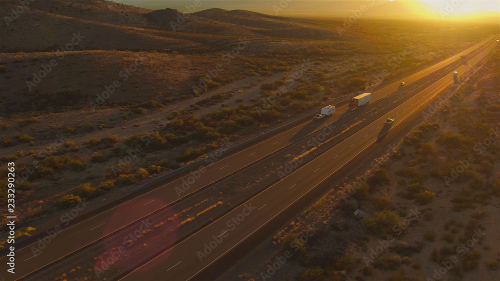 AERIAL: Cars and semi trucks driving on busy highway at summer sunset