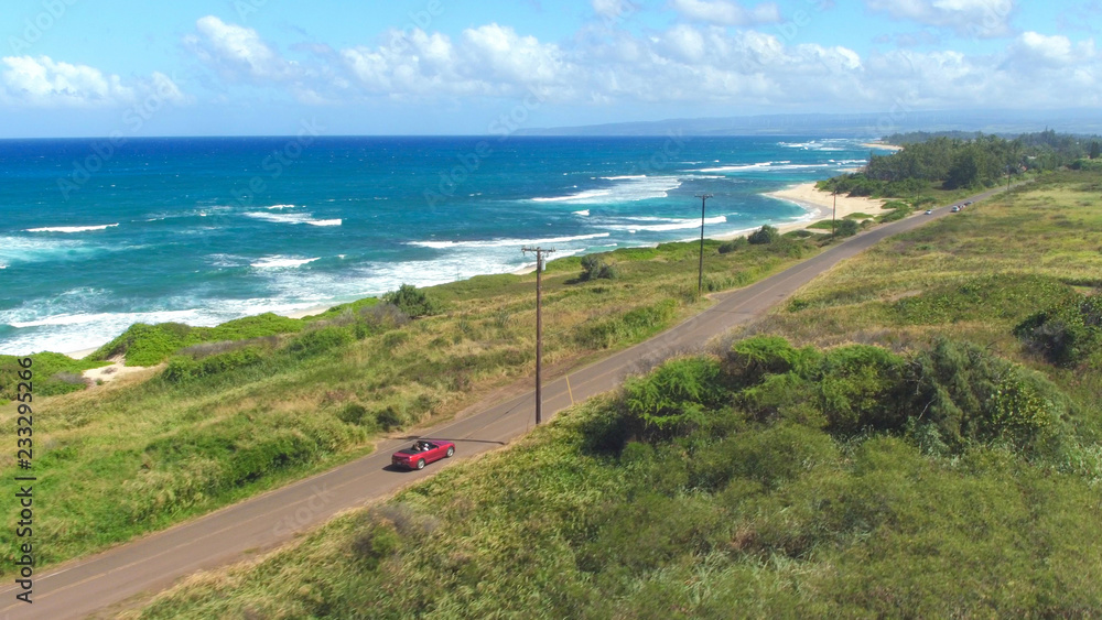 空中飞航：红色敞篷车沿着绿色夏威夷岛的海岸公路行驶