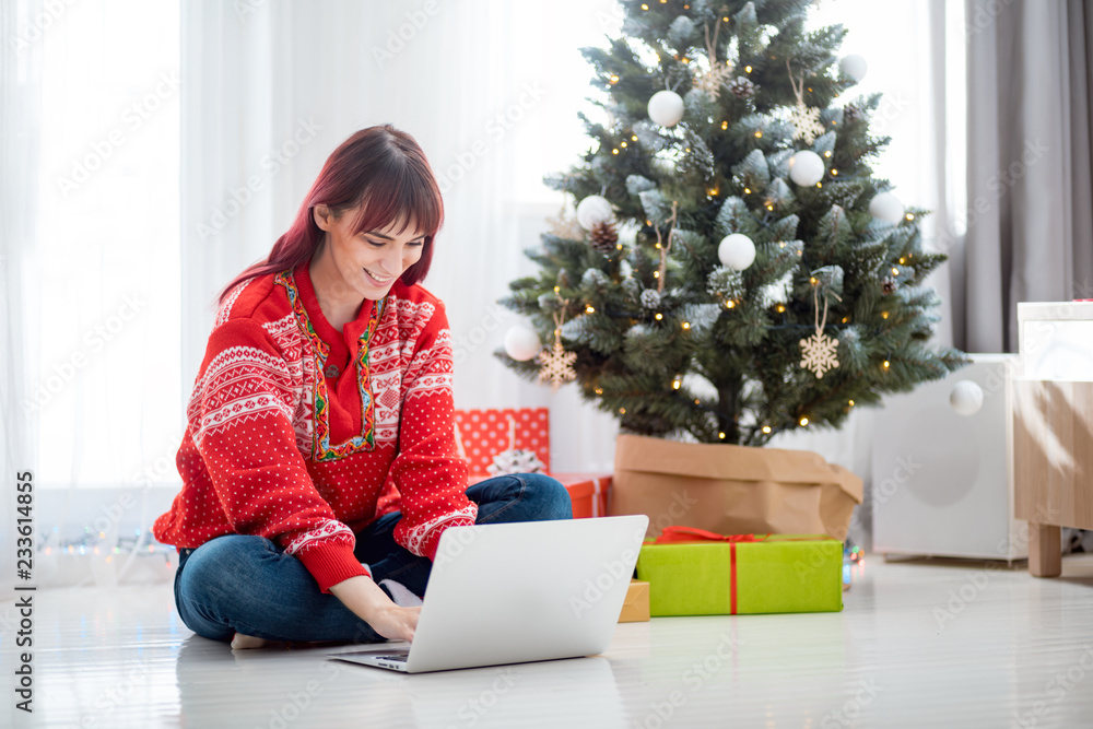 Young woman using laptop next to xmas tree, Christmas shopping online