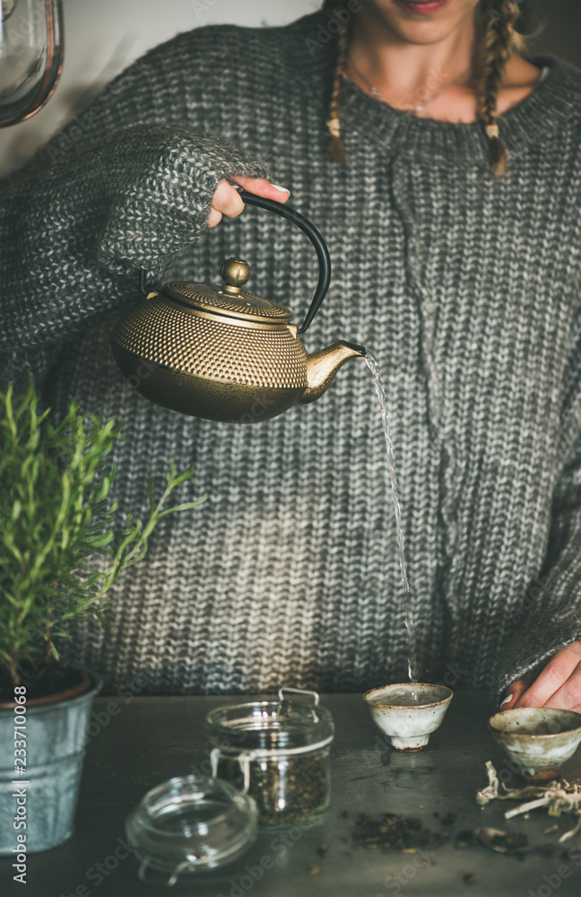 茶道。身穿灰色暖冬毛衣的年轻女性将金色铁壶中的绿茶倒入j中