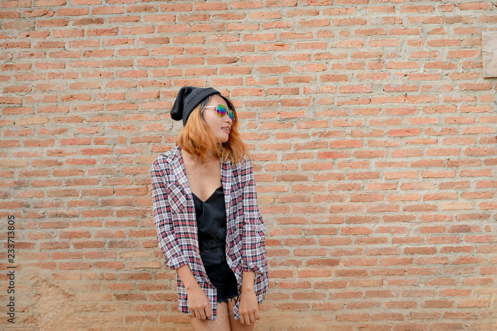 快乐的年轻时髦女人站在镇上的砖墙边。