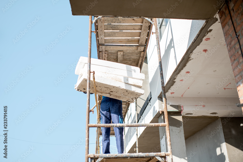 建筑工人用站在建筑脚手架上的泡沫板温暖建筑立面