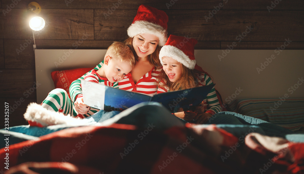 Merry Christmas! family mother reads to children book before bed in bed