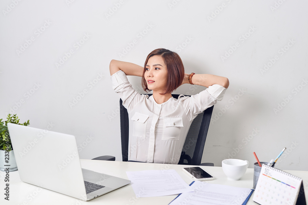 工作一天后，一位商务女性在办公室休息，双手向后仰在脑后