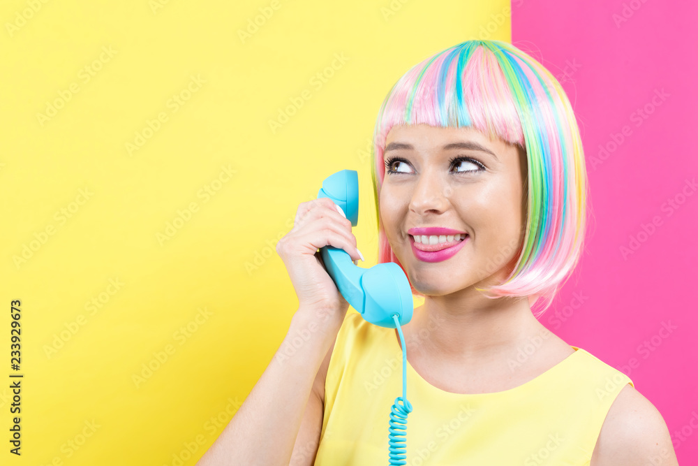 戴着彩色假发的年轻女子在黄色和粉色的背景下用复古的手机通话