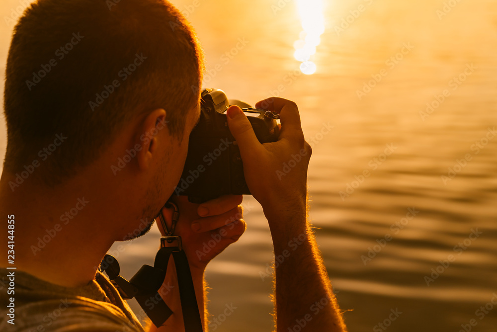 男性摄影师在户外用专业相机拍摄河边日落。男性照片