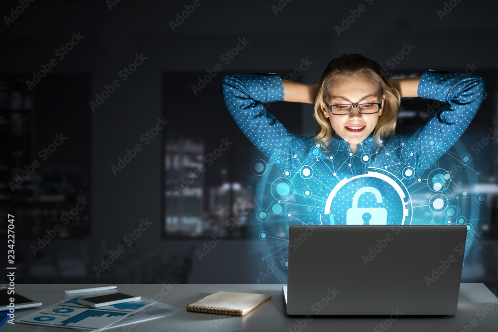美丽的金发女郎在黑暗的办公室里用笔记本电脑工作并获得网络访问权限