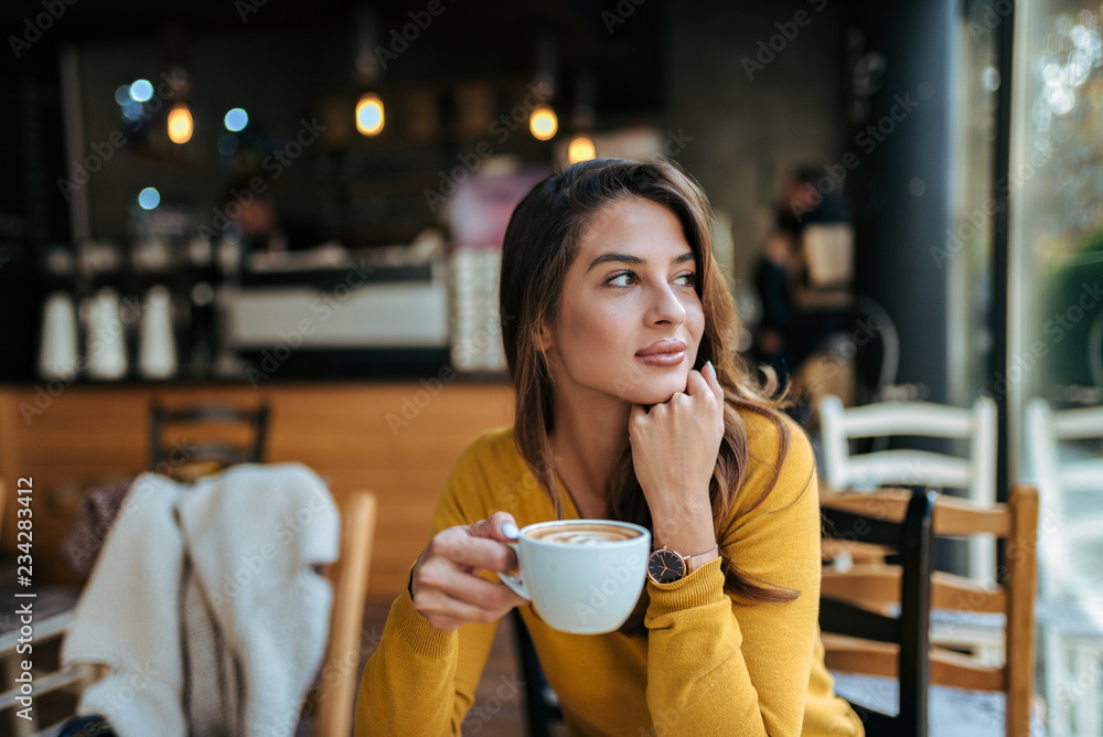 时尚的年轻女人在咖啡馆喝咖啡，目光移开。