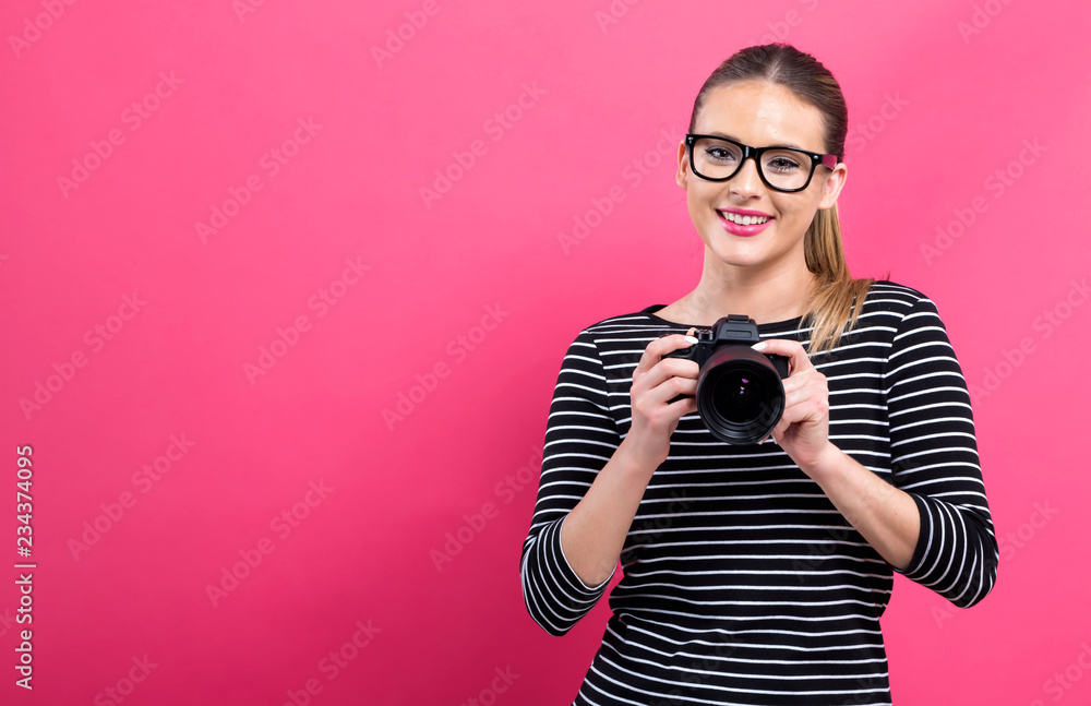 粉色背景下带着专业数码单反相机的年轻女性