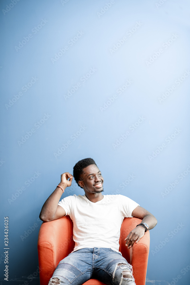 一个穿着白色t恤和牛仔裤坐在椅子上的非洲年轻人的肖像