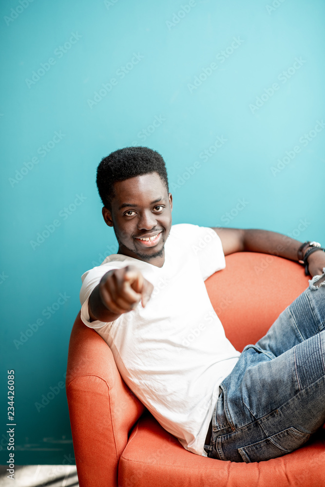 一个穿着白色t恤和牛仔裤坐在椅子上的年轻非洲男子的情感肖像