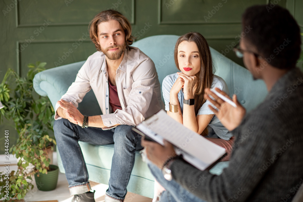 一对严肃的年轻夫妇在心理咨询期间坐在舒适的沙发上拜访心理学家