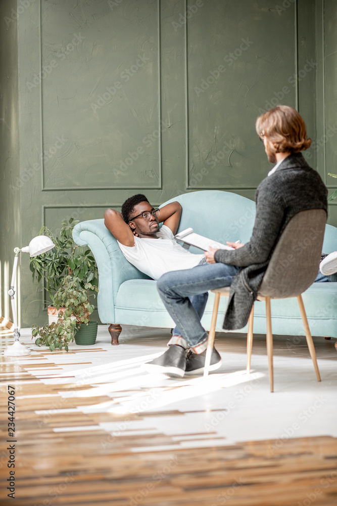 年轻的非裔男子与躺在舒适的沙发上的心理学家进行了严肃的交谈