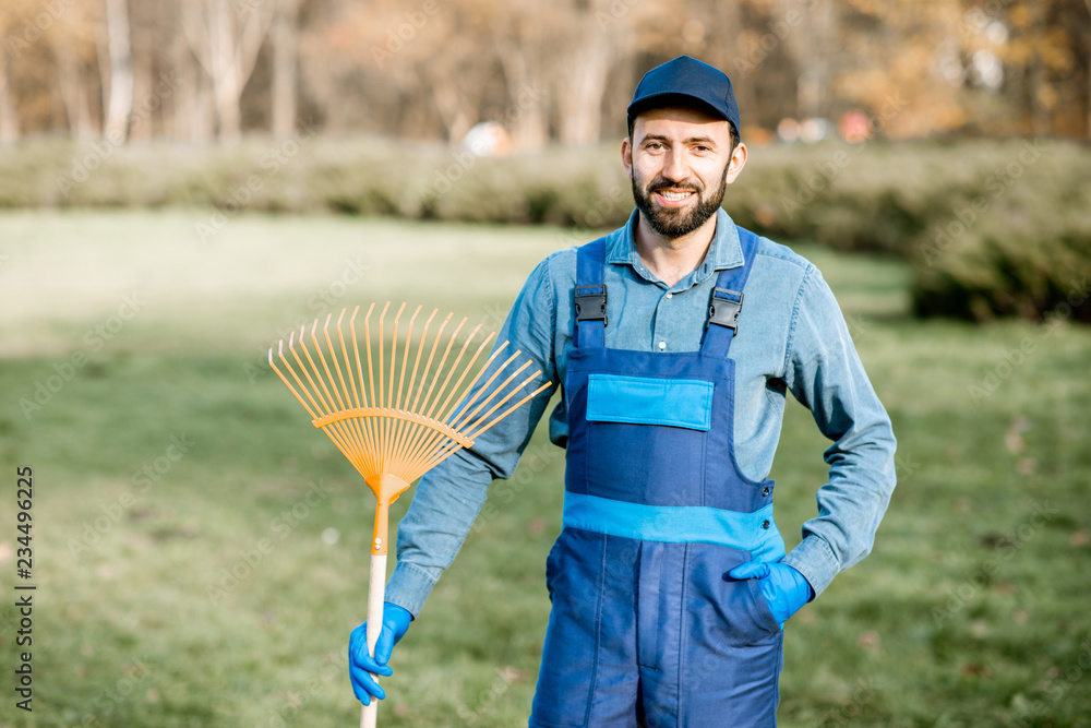 一位身穿制服、手持耙子站在花园里的专业男性清扫工或园丁的肖像