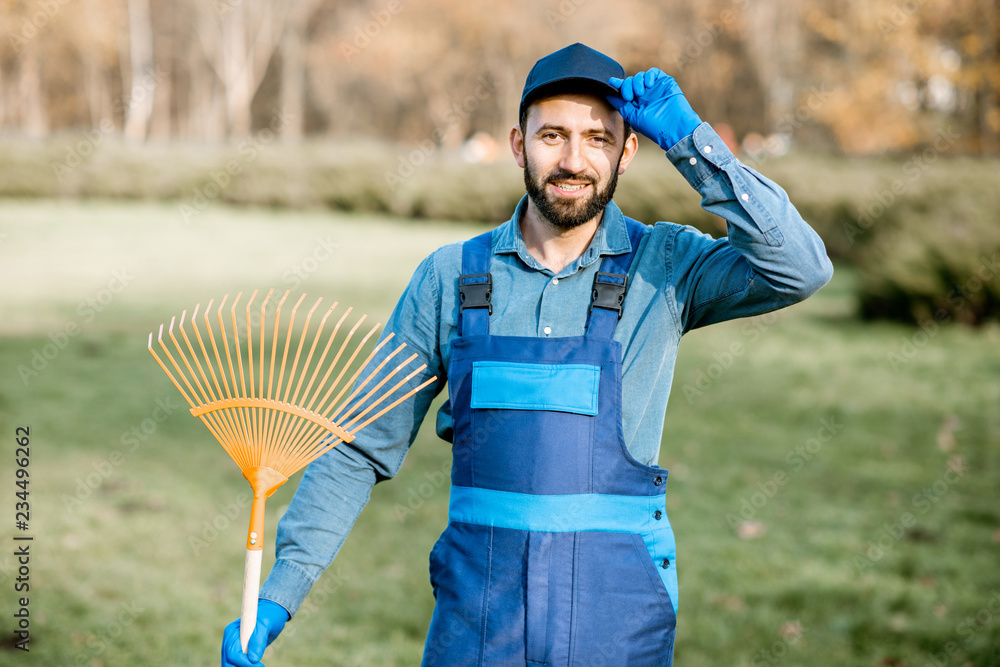 一位身穿制服、手持耙子站在花园里的专业男性清扫工或园丁的肖像
