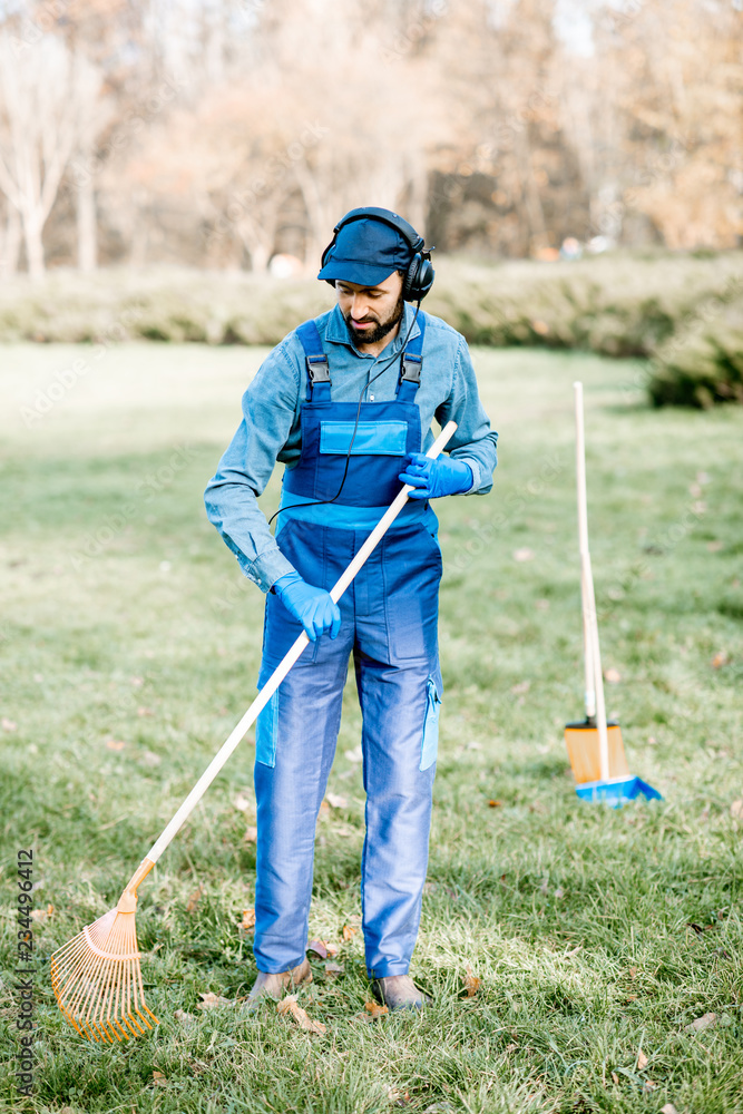 穿着制服的专业男性清扫工或园丁在清扫时戴着耳机听音乐