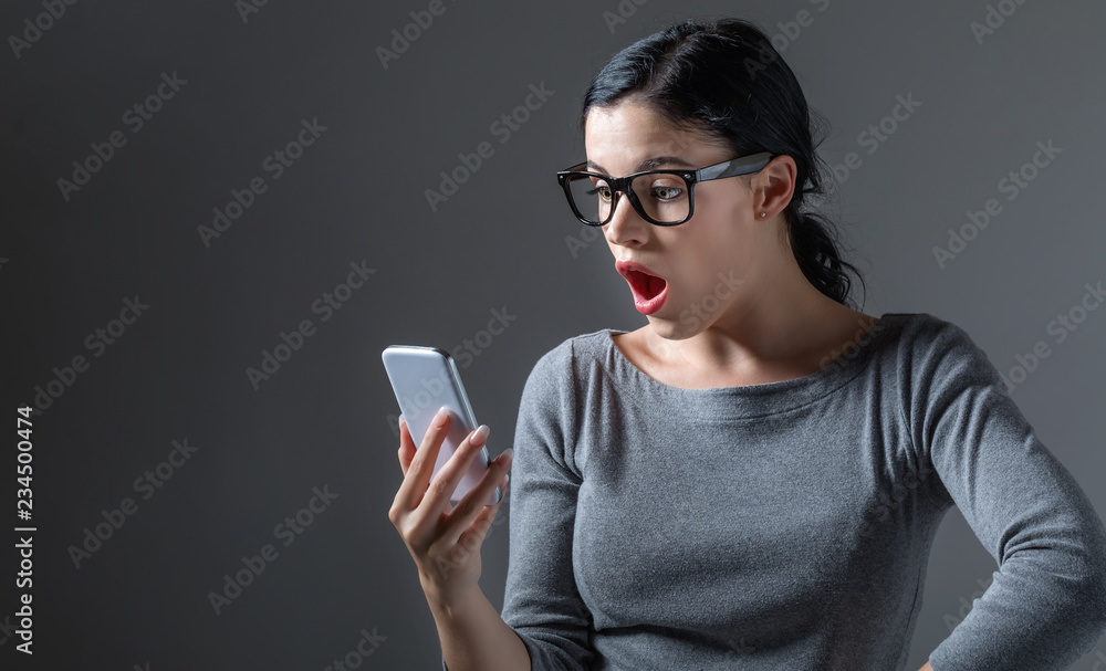 一名年轻女子在灰色背景下盯着手机