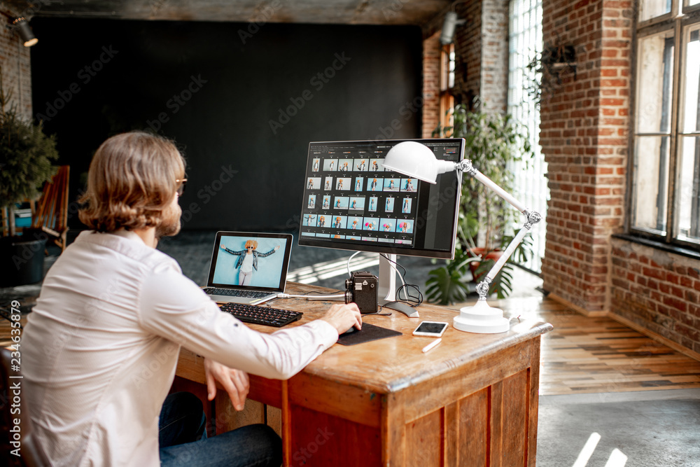 年轻的男性摄影师用两台电脑拍摄坐在工作场所的女性肖像