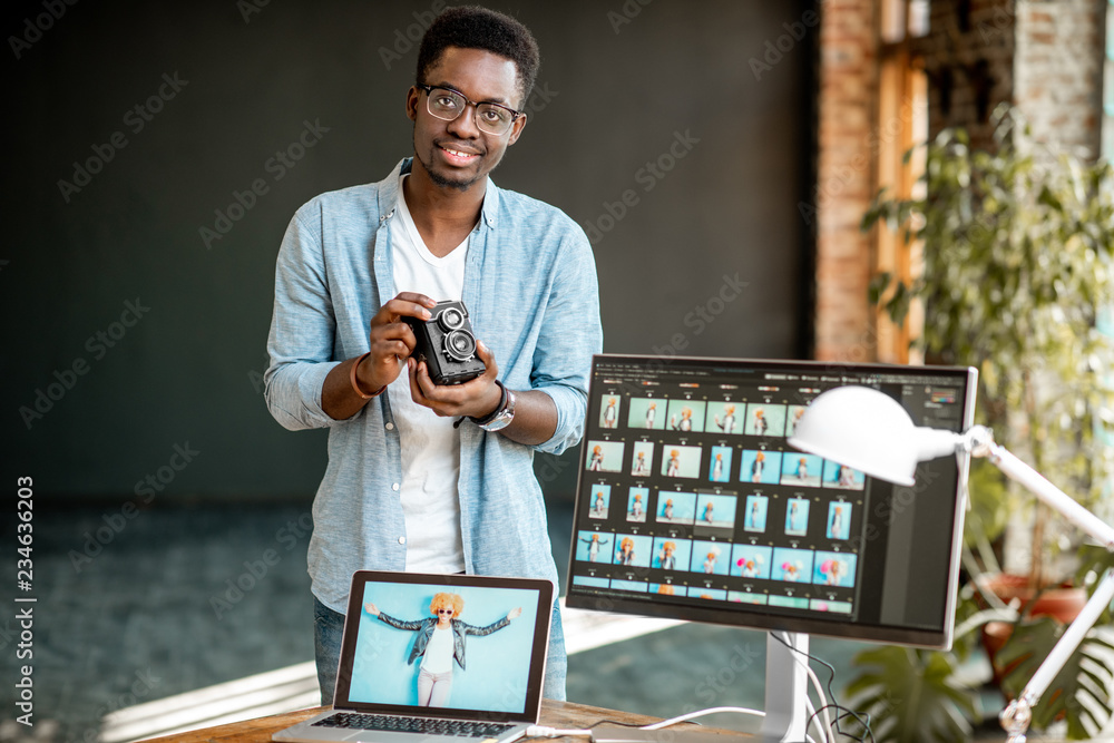 一位年轻的非洲裔摄影师拿着复古相机站在工作场所附近的肖像