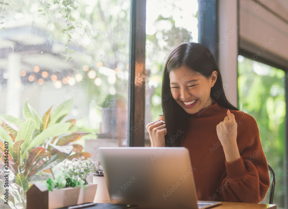 年轻的亚洲女性用笔记本电脑庆祝成功或快乐姿势