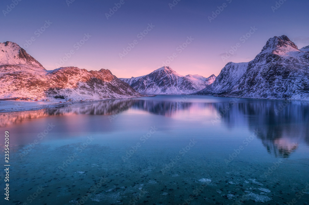 黄昏时，白雪皑皑的山脉和水中倒影的彩色天空的鸟瞰图。冬季景观