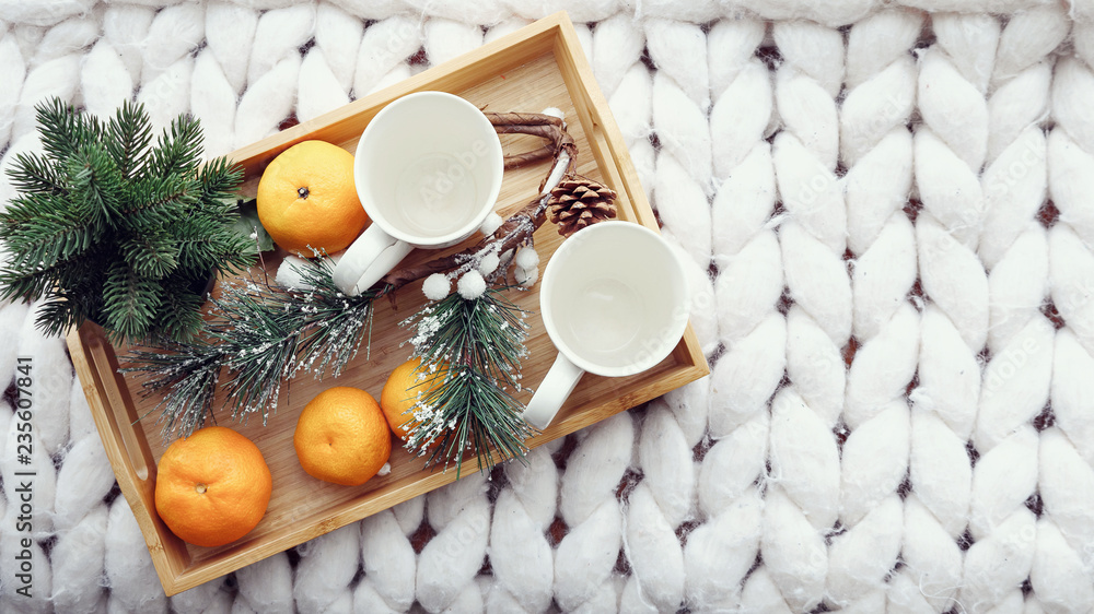 两个带有节日装饰的白色杯子、橘子、松果、冷杉和松膜的俯视图