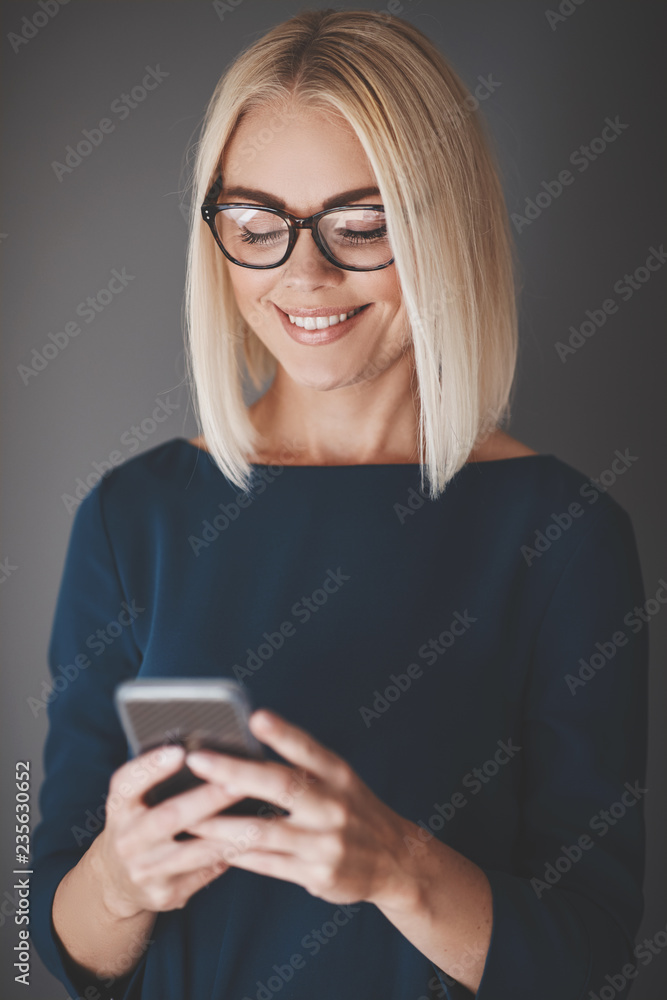 Smiling young businesswoman using her cellphone against a gray b