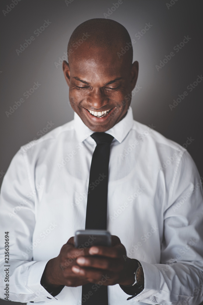 Smiling African businessman using his cellphone against a gray b