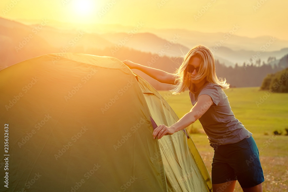 快乐的女人张开双臂，待在阳光下群山环绕的帐篷附近
