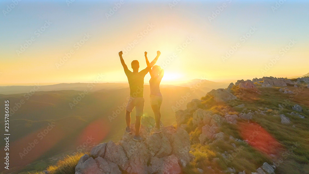 空中：徒步旅行者夫妇在日落时分登顶后伸出双臂。