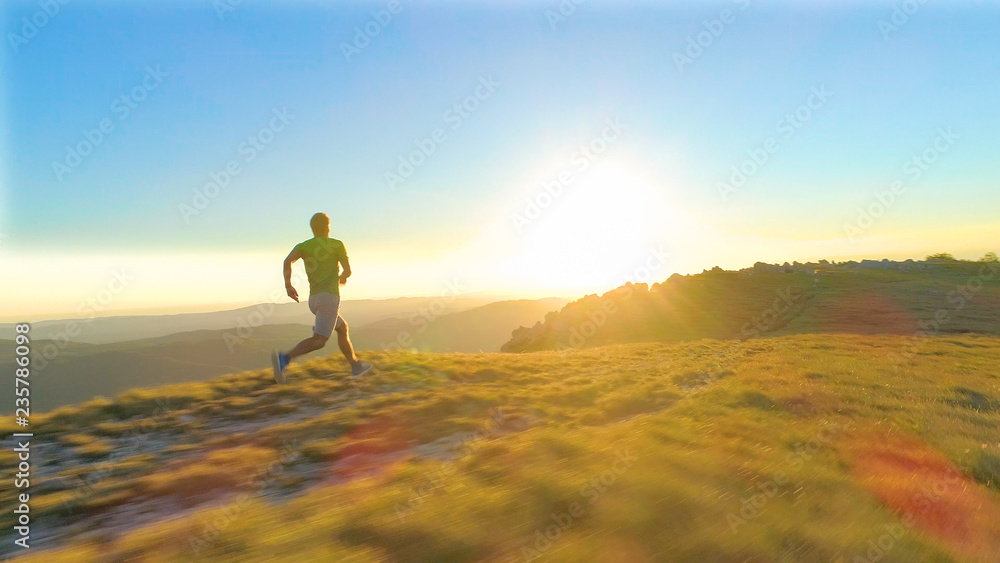 LENS FLARE：一个阳光明媚的早晨，一个运动型年轻人从长满草的小山上飞奔而下