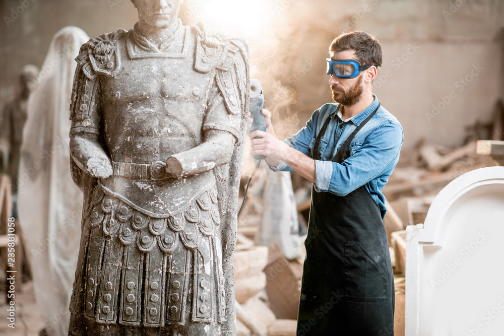 一位英俊体贴的雕塑家的肖像，穿着蓝色t恤和围裙，与石雕一起工作o