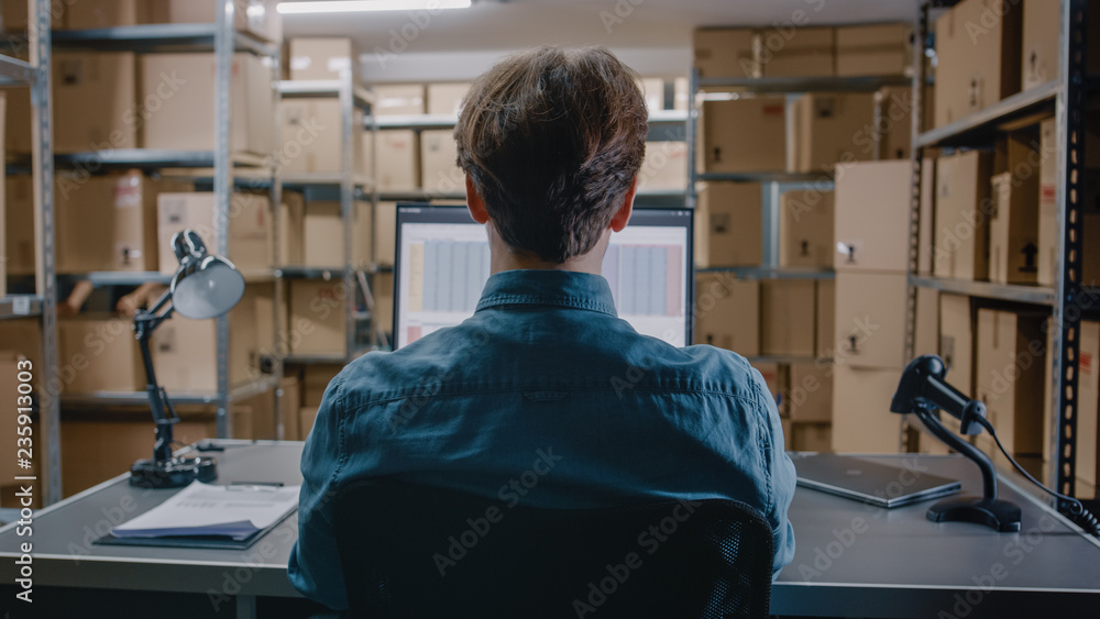 仓库库存经理坐在他的Des工作时在个人电脑上使用电子表格