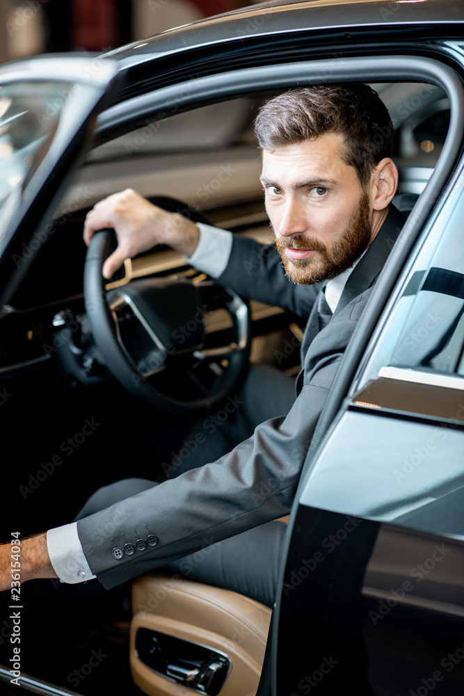 一位英俊的商人坐在展厅豪华汽车的驾驶座上的肖像